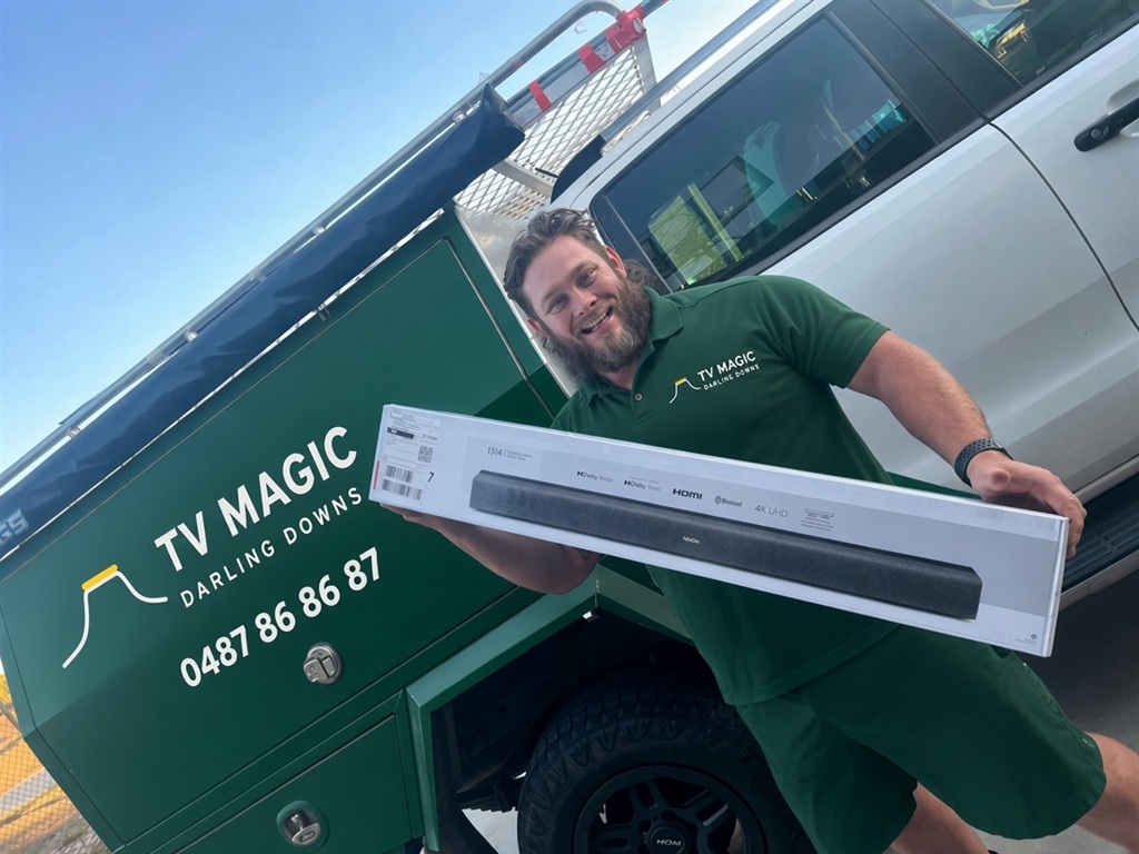 Nick grinning beside his green work ute, holding a boxed sound bar